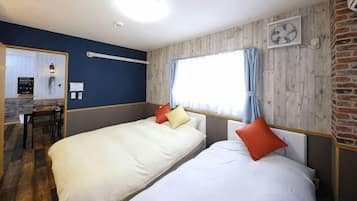 A hotel room with two beds, a wooden wall, a window with curtains, and a small table with chairs.