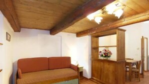 Ein gemütliches Zimmer mit Holzbalkendecke, einer Couch, einem kleinen Tisch mit Blumenvase und einem Essbereich.