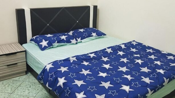 A bed with a blue and white star-patterned bedspread, a wooden nightstand, and a green striped pillow. - Homestay Che Wan (Kuala Kuantan)