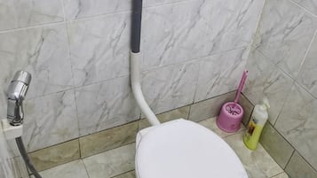 A bathroom with a white toilet, a shower hose, a pink cleaning brush, and a bottle of cleaning liquid.