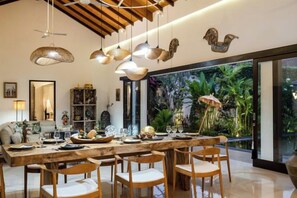 A dining area with a long wooden table, multiple chairs, hanging pendant lights, and a large aquarium with tropical plants. - Jami 4BR PoolVilla, a Serenity Steps from theBeach (Bali)