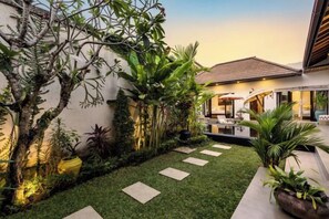 A well-maintained garden with a patio area, a dining setup, and a variety of plants. - Jami 4BR PoolVilla, a Serenity Steps from theBeach (Bali)
