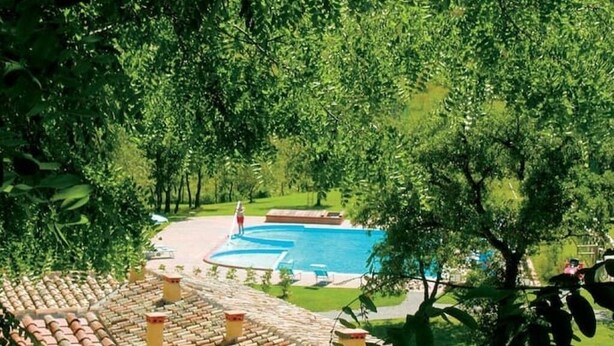 A swimming pool surrounded by lush greenery, with a tiled roof and outdoor seating area. - Apartment 26 with 1 Bedroom and Bathroom - Simple and Comfortable (Castel del Piano)