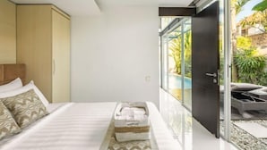 Ein modernes Hotelzimmer mit einem Bett, einem kleinen Nachttisch und einer Glastür, die auf einen Balkon mit Gartenmöbeln führt.
