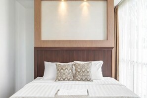 A bed with a wooden headboard, patterned pillows, and a bedside table with a basket. - Villa De Luca By Aishwarya Bali International (Bali)