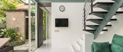 A modern interior with a staircase, a flat-screen TV, and a green sofa.