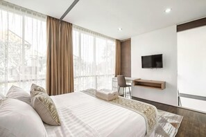 A hotel room with a large bed, a desk, a chair, a TV, and a window with curtains. - Villa De Luca By Aishwarya Bali International (Bali)