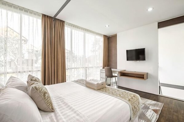 A hotel room with a large bed, a desk, a chair, a TV, and a window with curtains. - Villa De Luca By Aishwarya Bali International (Bali)
