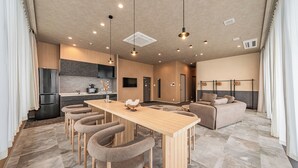 A modern kitchen with a central island, bar stools, and a dining table. There is a sofa and a TV in the living area. - Apartment Hotel 11 Shinimamiya 3 (Osaka)