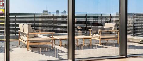 A modern outdoor seating area with tables and chairs, large windows, and a view of the cityscape.