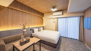 A modern hotel room with a wooden ceiling, a bed with a white mattress, a grey sofa, a small wooden table with a box and a vase, and a window with curtains.