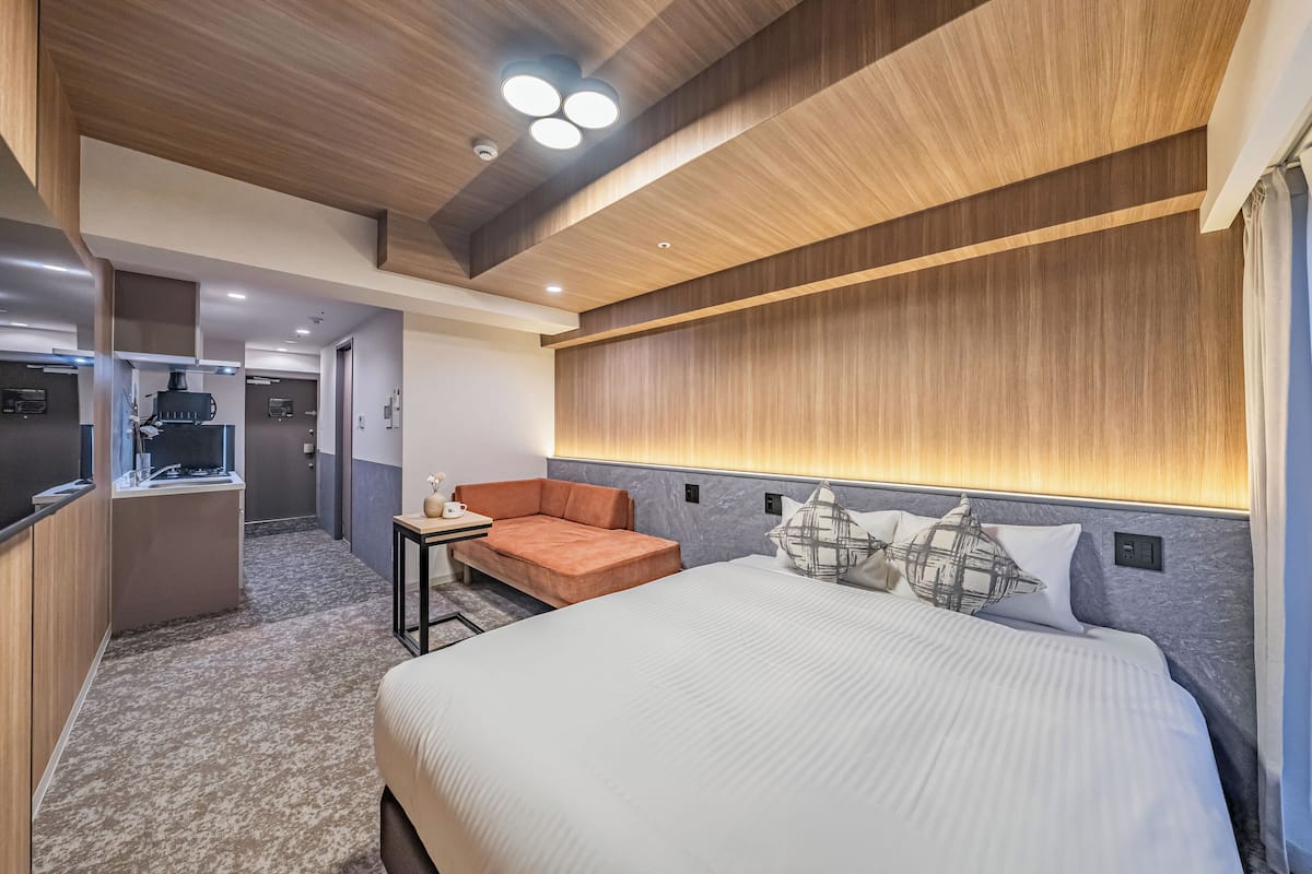 Una habitación de hotel moderna con una cama grande, un sofá, una mesita y una kitchenette.