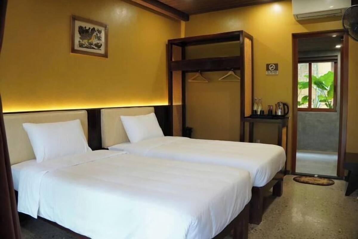 Ein Hotelzimmer mit zwei Betten, einem Holzkopfteil, einem kleinen Tisch mit Kaffeemaschine und Blick auf Grünfläche.