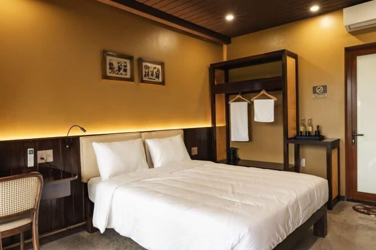 Ein Hotelzimmer mit Bett, Schreibtisch, Stuhl, Spiegel und Garderobe.