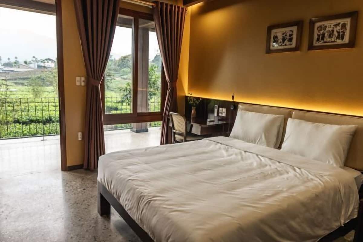 Ein Schlafzimmer mit Bett, Vorhängen, Schreibtisch und Blick auf eine grüne Landschaft.