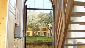 A view through an open door into a courtyard with a building, trees, and a clear sky. - Apartment 29 Surrounded by Tranquility (Castel del Piano)