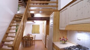 A kitchen with wooden cabinets, a gas stove, and a dining area with a table and chairs. - Apartment 29 Surrounded by Tranquility (Castel del Piano)