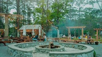An outdoor dining area with stone fire pits, wooden tables, and umbrellas.