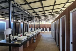Une rangée de petits espaces individuels, chacun équipé d’un lavabo et d’un miroir, un long comptoir avec une lampe, et des portes sur le côté droit.