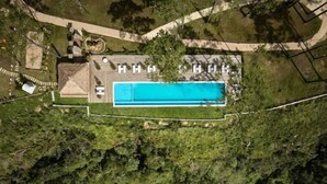 Vista aérea de una propiedad con piscina, un patio cubierto y un jardín ajardinado.