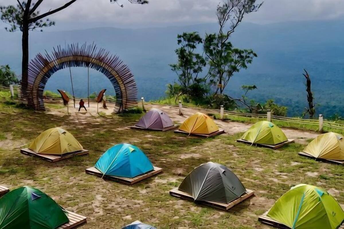 A series of colorful tents arranged on a grassy area with a view of the sea and a wooden arch structure.