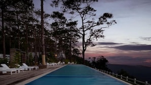 Una piscina con sillones de descanso y vistas a la montaña al atardecer.