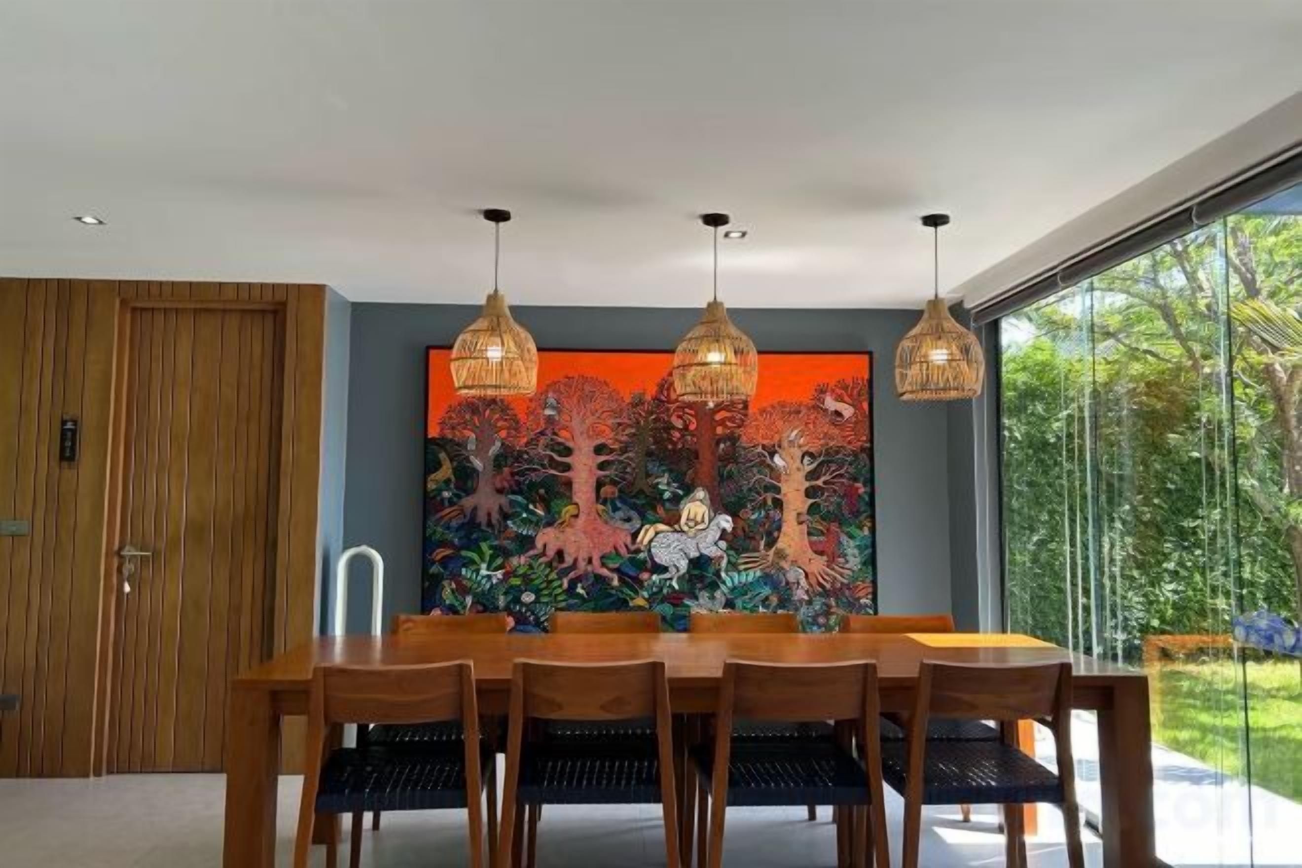 Un comedor con una mesa y sillas de madera, un cuadro abstracto grande y lámparas colgantes.