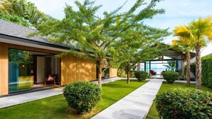 A modern house with a glass facade, a well-maintained lawn, and a pathway leading to a seating area. - Baan Talay BeachFront Pool Villa A (Koh Samui)