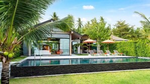 A modern house with a swimming pool, surrounded by lush greenery and palm trees. - Baan Talay BeachFront Pool Villa A (Koh Samui)