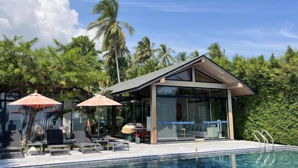 Ein moderner Poolbereich mit Liegestühlen und Sonnenschirmen, umgeben von üppiger Vegetation und Palmen.