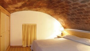 A bedroom with a brick ceiling, a wooden door, a bed with white bedding, and a lamp on a bedside table. - Apartment 39 for Families or Couples (Castel del Piano)