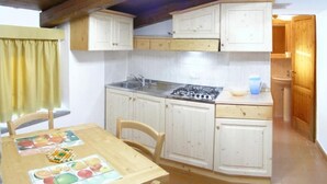 A compact kitchen with white cabinets, a gas stove, and a dining table with placemats. - Apartment 21 with 1 Bedroom - Perfect for 4 Travelers (Castel del Piano)