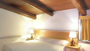 A bedroom with a wooden headboard, a single bed, two bedside tables with lamps, and a window with curtains. - Apartment 21 with 1 Bedroom - Perfect for 4 Travelers (Castel del Piano)