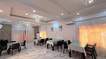 A dining area with marble flooring, tables, chairs, and a chandelier.