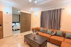 A hotel room with a sofa, a coffee table, a bed, and a sliding door leading to another room. - Star Wish Business Hotel (Ikeja)