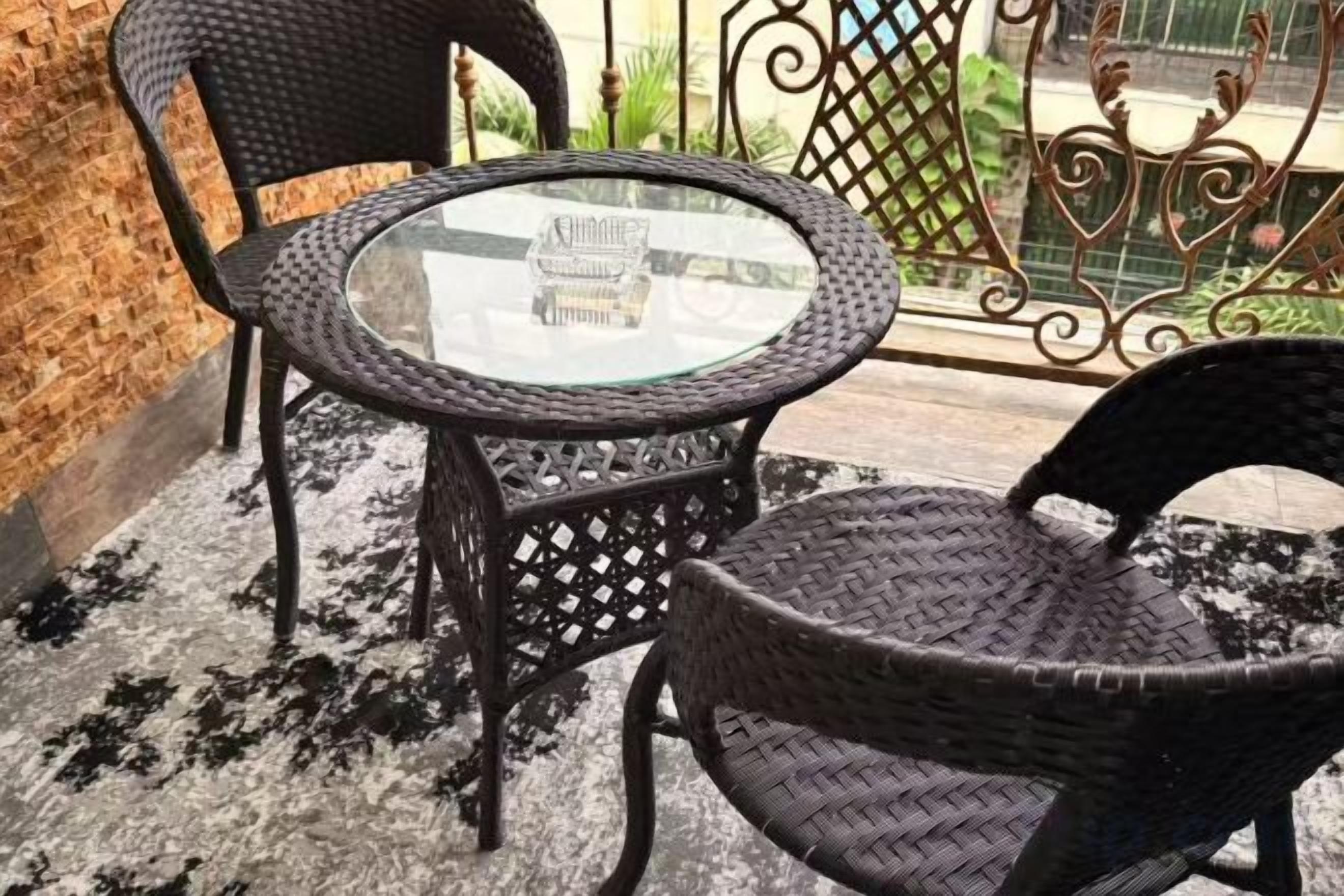 Una mesa redonda de vidrio con sillas de mimbre en un balcón.