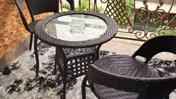 Una mesa redonda de vidrio con sillas de mimbre en un balcón.