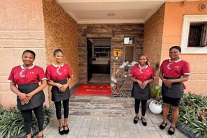 Four individuals in red uniforms standing in front of a building entrance with a red carpet and a sign indicating 'House 1'. - Star Wish Business Hotel (Ikeja)