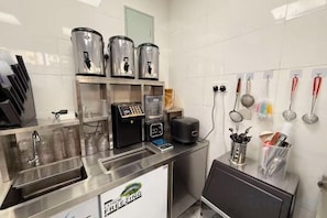 A commercial kitchen with stainless steel appliances, a coffee machine, and various utensils on the wall. - Star Wish Business Hotel (Ikeja)