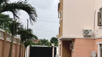 Una calle residencial con entrada vigilada, palmeras y edificios con unidades de aire acondicionado.