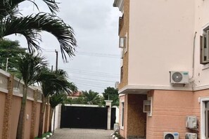 A residential street with a gated entrance, palm trees, and buildings with air conditioning units. - Star Wish Business Hotel (Ikeja)