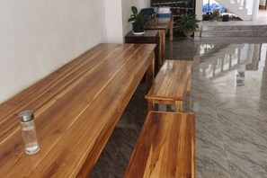 A wooden bench and table in a room with a polished floor, a potted plant, and a window in the background. - V V Guesthouse (Vang Vieng)