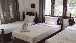 Habitación de hotel con tres camas de madera, cada una con sábanas y almohadas blancas, una mesita de noche pequeña y una ventana con cortinas.