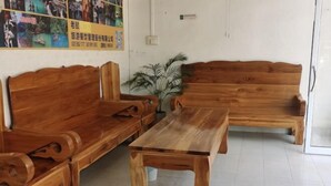 Zona de recepción con bancos de madera, una mesa de centro, una planta en maceta y una pared con carteles.