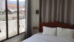 Una habitación de hotel con un ventanal grande, una cama con ropa de cama blanca y un cabecero de madera.