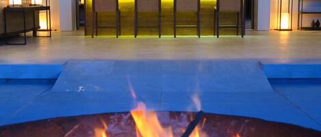 Zona de piscina con un pozo de fuego al frente y un área de bar con asientos al fondo.