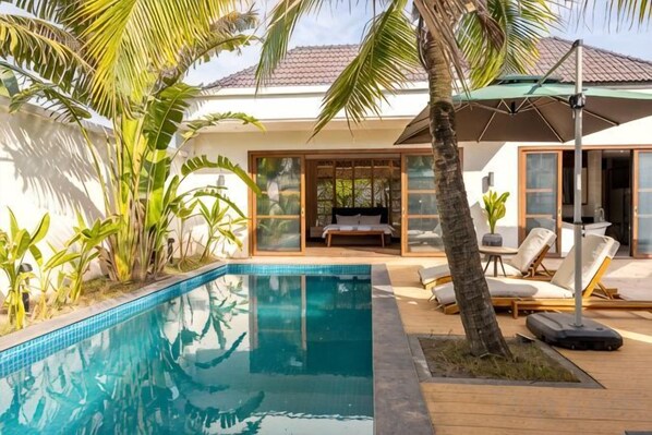 A pool area with a lounge chair, a table, and a palm tree. - Ream YoHo Resort (Prey Nob)
