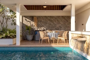 A poolside area with a dining table and chairs, a built-in barbecue, and a stone wall backdrop. - Ream YoHo Resort (Prey Nob)