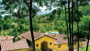 A yellow building with a tiled roof, surrounded by trees and a view of a green landscape. - Apartment 22 for 4 Guests (Castel del Piano)