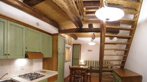 A kitchen with green cabinets, a wooden staircase, and a dining area with a table and chairs. - Apartment 22 for 4 Guests (Castel del Piano)